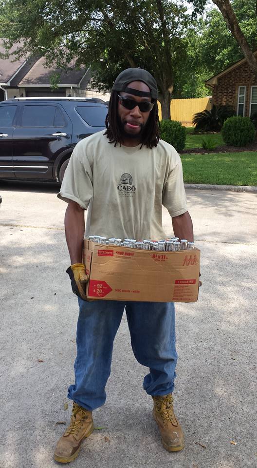 Photo of a random African American dressed in dirty work cloths, holding a cardboard box containing 30 Corona beer bottles